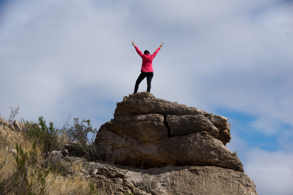 Person in red jacket standing on rock with arms in air