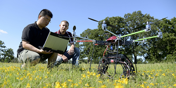 Two students programming a drone in a field
