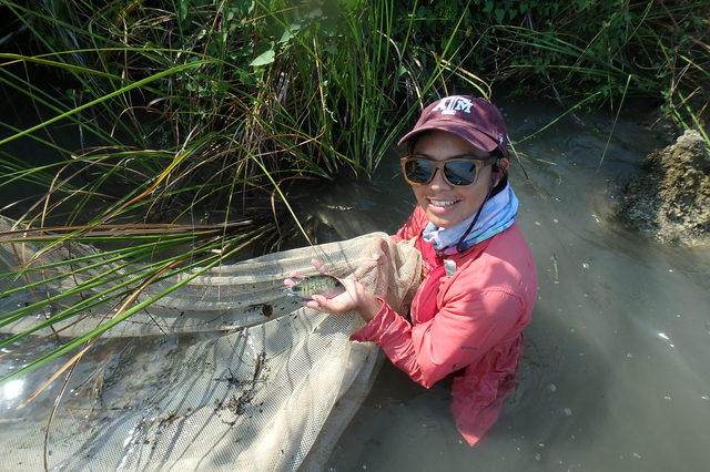 Yasmin Quintana standing waist-high in a creek, holding a fishing net