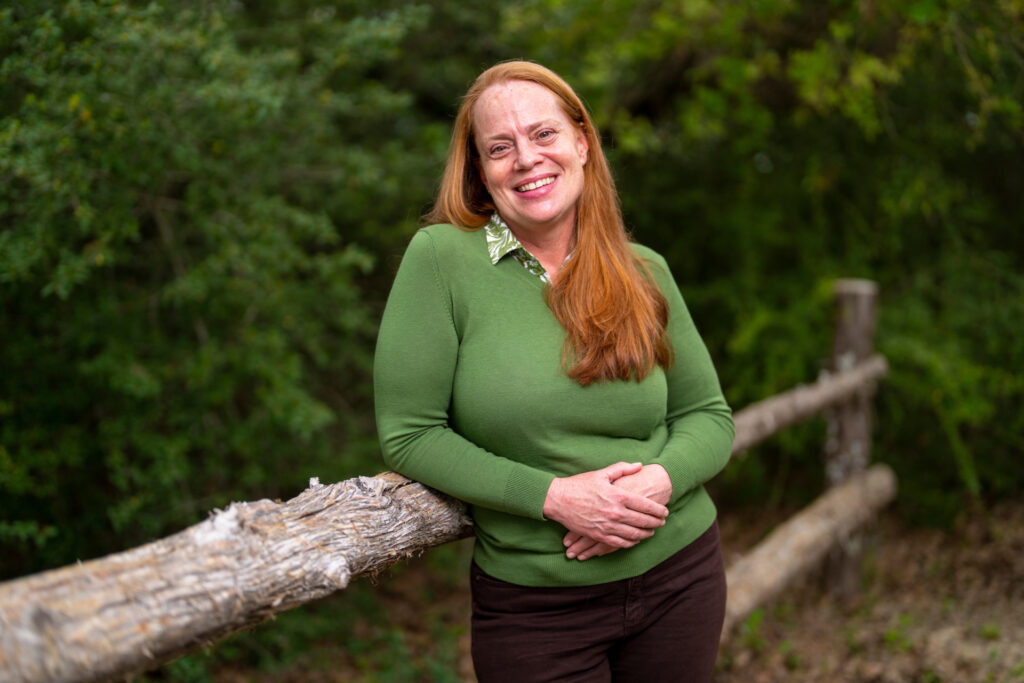 Head and shoulders of Dr. Katy Gonder standing surrounded by lush green trees.
