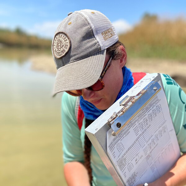 Person wearing sun protection holding a clipboard with notes on it