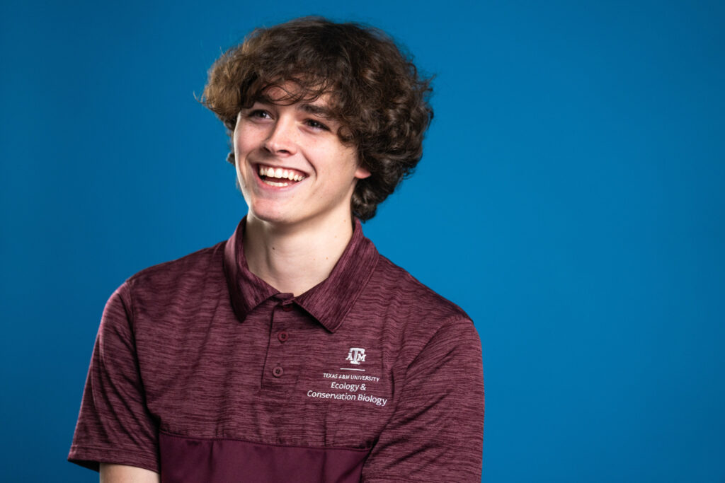 Student wearing a TAMU polo smiling with a blue background.